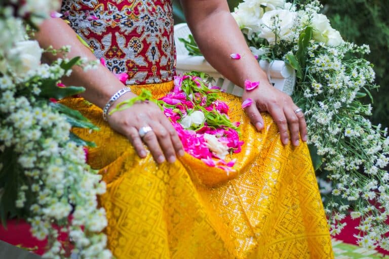 Détail d'une femme balinaise portant un sarong jaune et une kebaya traditionnelle lors d'une cérémonie intime avec Heaven Collection, entourée d'offrandes florales.