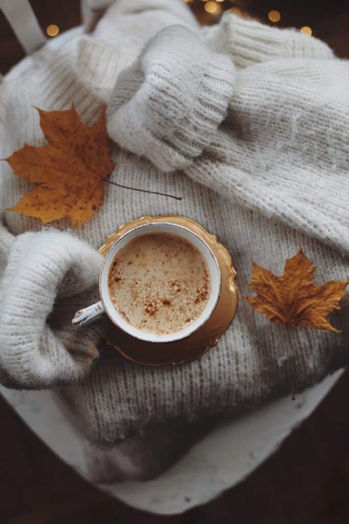 Tasse de boisson chaude tenue dans des mains emmitouflées aux premiers frissons de la foliage season.