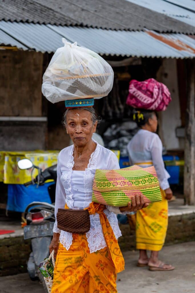 Femme balinaise en tenue traditionnelle portant des offrandes colorées lors d'une fête locale à Bali