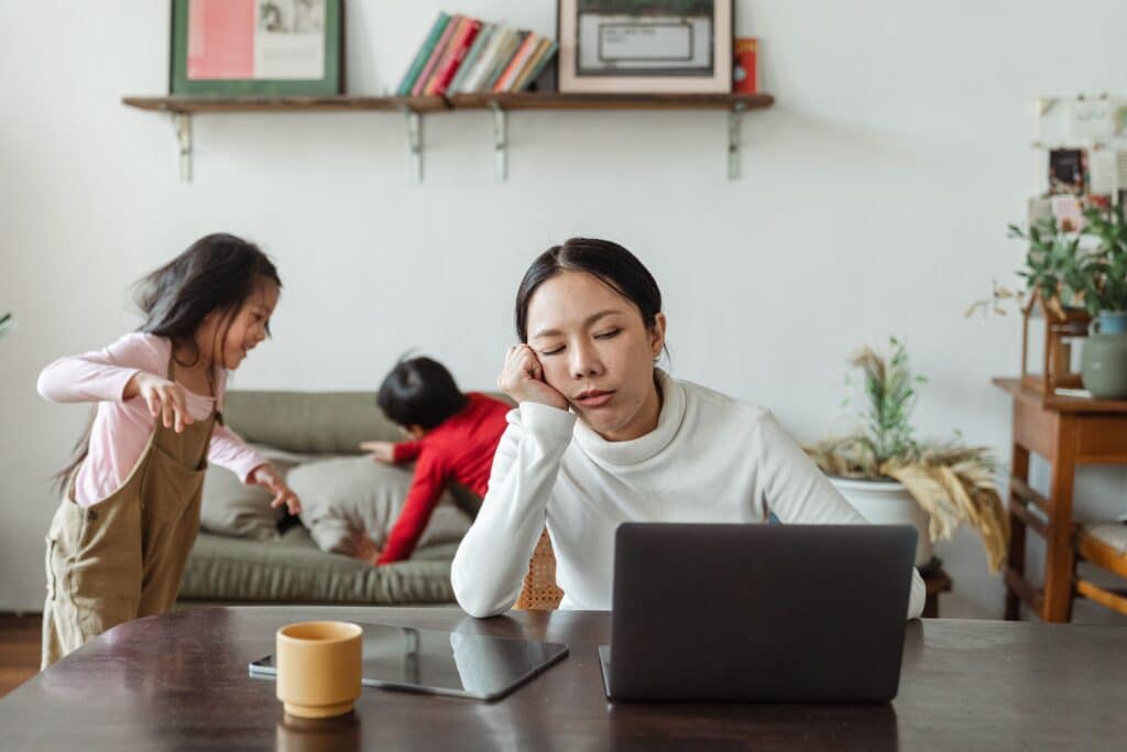 Maman épuisée travaillant sur ordinateur face au tourbillon du quotidien familial.