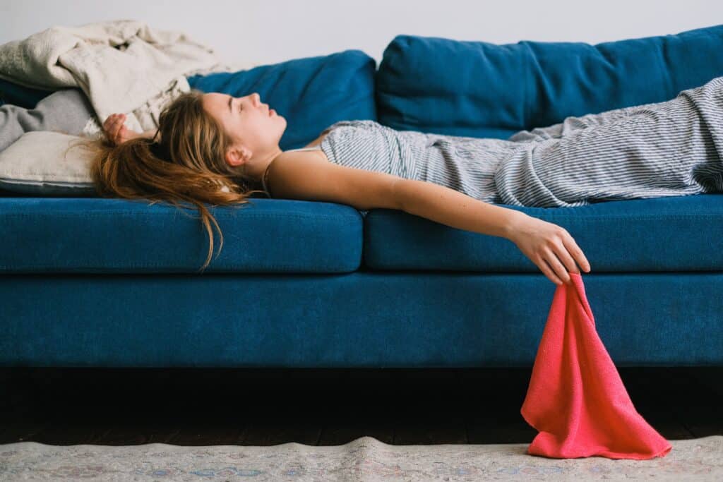 Maman fatiguée allongée sur un canapé bleu, illustrant la charge mentale et le besoin de lâcher prise.