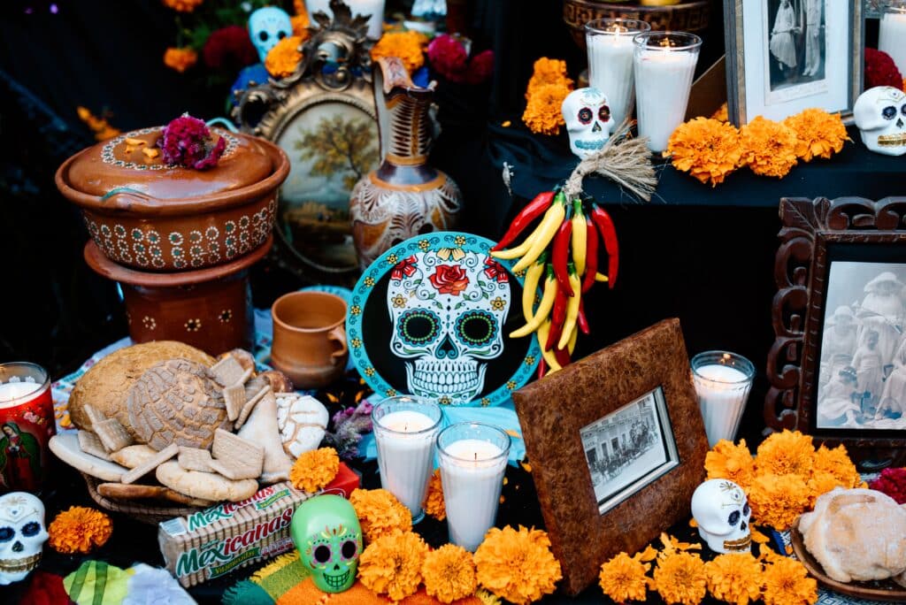 Composition détaillée d'un autel (ofrenda) de salon, avec des cadres photo, des bougies, des têtes de mort en sucre décorées, des piments séchés, du Pan de Muerto et des fleurs de cempasúchil.