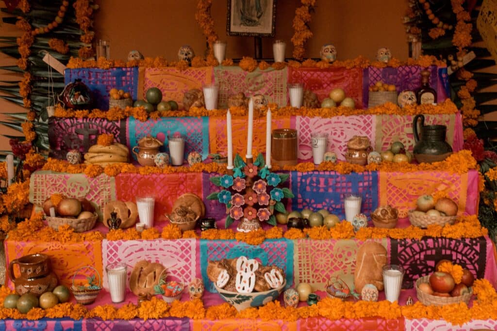 Vue détaillée d'un autel (ofrenda) traditionnel à plusieurs niveaux, couvert de nappes colorées, de guirlandes de papel picado, de Pan de Muerto, de fruits, de bougies et de nombreuses fleurs d'œillet d'Inde.