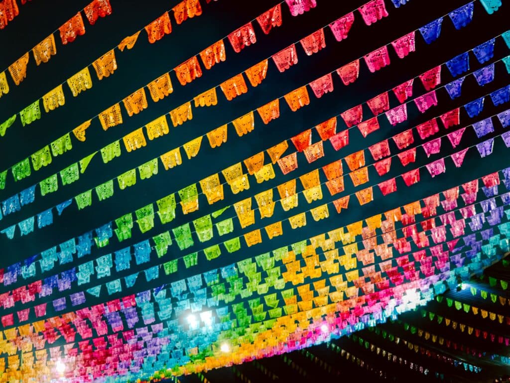 Perspective plongeante sur des centaines de guirlandes de papel picado colorées tendues en diagonale au-dessus d'une rue, créant un ciel de motifs découpés multicolores la nuit.