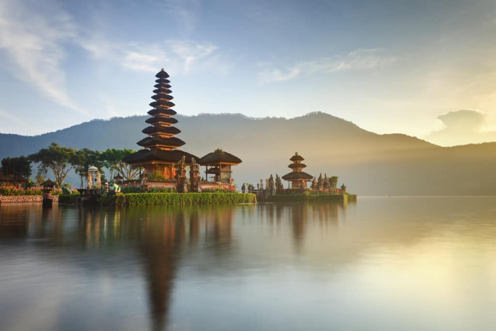 « Vue panoramique et feutrée du temple Pura Ulun Danu Bratan sur le lac à Bali au lever du soleil, une expérience sur-mesure Heaven Collection.