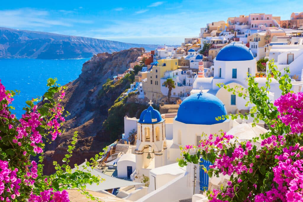 Églises aux dômes bleus emblématiques et bougainvilliers fuchsia surplombant la caldeira à Santorin, voyage sur-mesure en duo Heaven Collection.