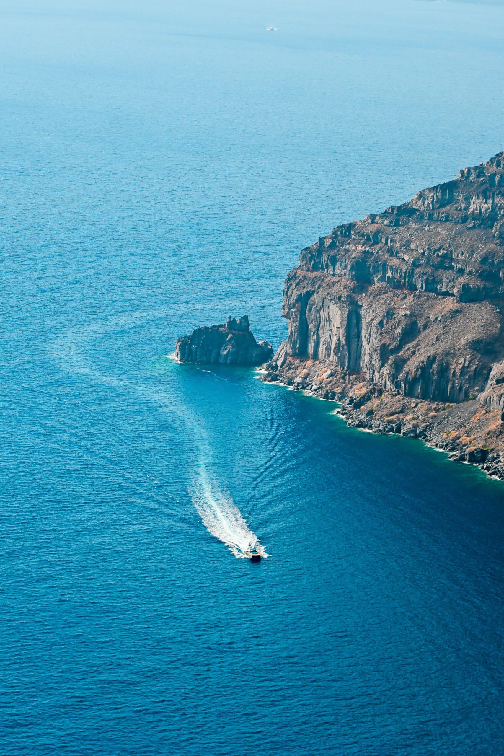 Bateau naviguant dans les eaux profondes et azurées de la caldeira volcanique de Santorin, expérience exclusive Heaven Collection.