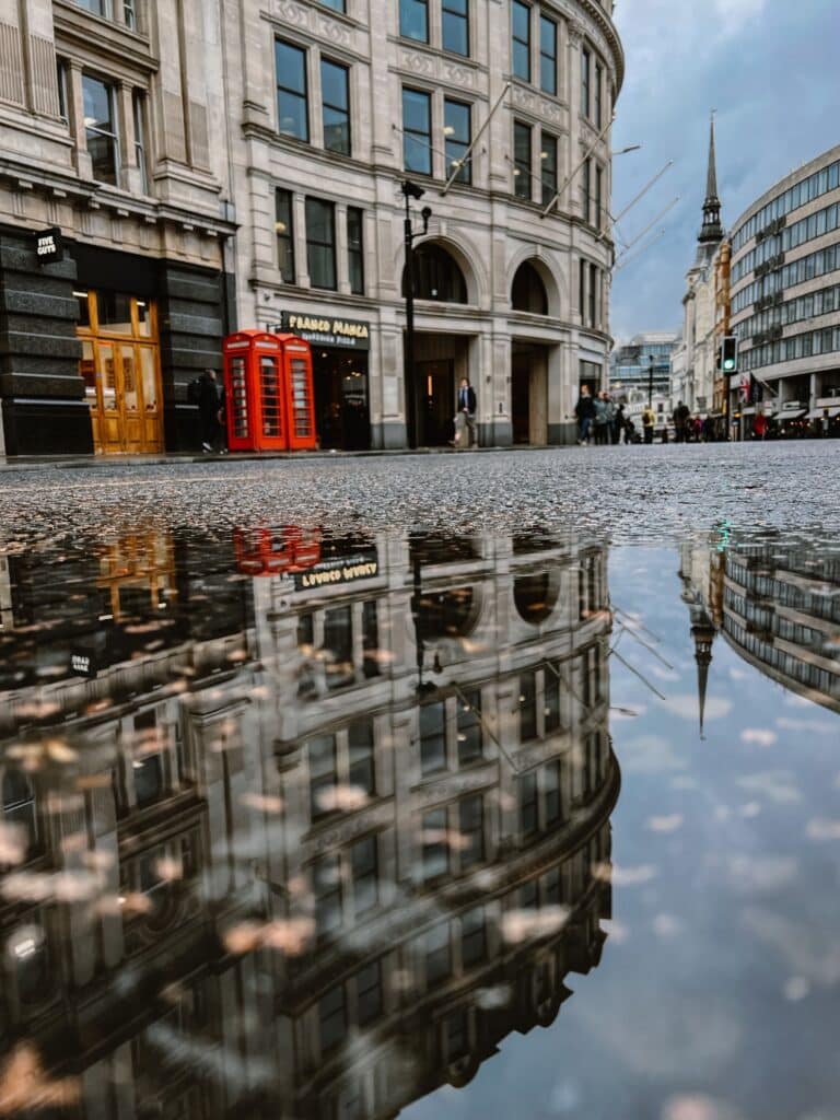 Cabines téléphoniques rouges typiques et architecture historique se reflétant dans l'eau, une ambiance cinéma pour un voyage à deux dans la Londres royale.