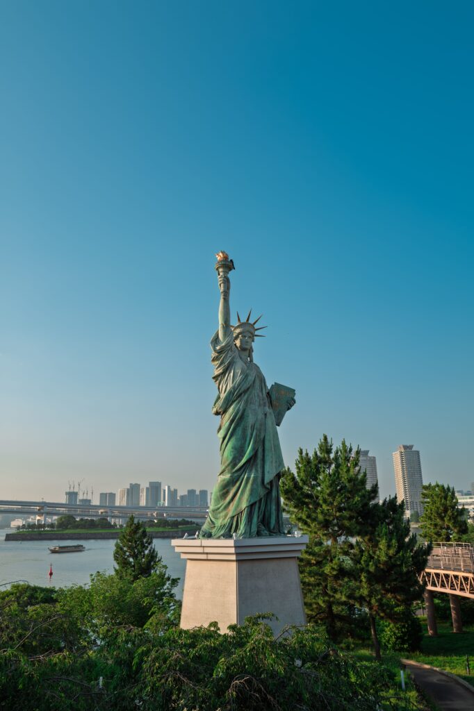 Statue de la Liberté se dressant face à la skyline de New York sous un ciel bleu, symbole intemporel d'évasion imaginé par Heaven Collection.