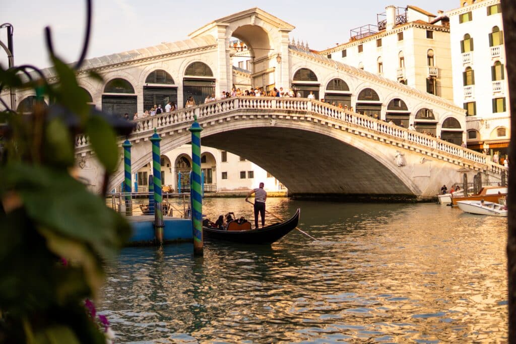 Texte alternatif : Vue imprégnée de romantisme sous le Pont du Rialto à Venise, où les gondoles offrent une escapade inoubliable pour les couples.