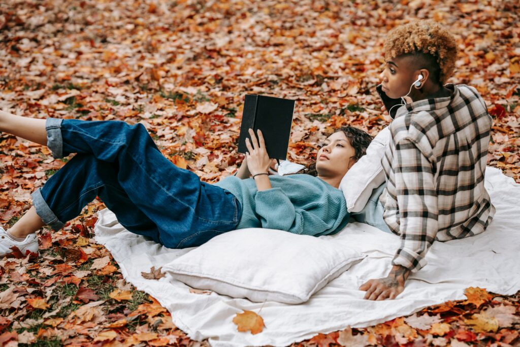Duo profitant d’un moment de détente en plein air sur une couverture au milieu des feuilles d’automne.