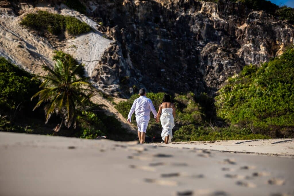 Deux personnes marchant ensemble sur une plage bordée de végétation et de falaises.
