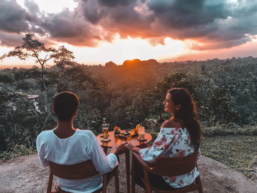 Deux personnes attablées face à un paysage tropical au coucher du soleil.