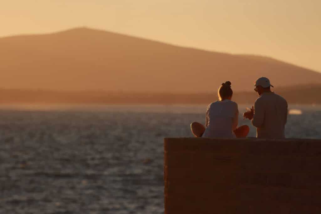 Deux personnes assises face à une ville baignée par la lumière du coucher de soleil.