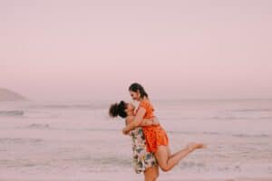 Duo enlacé au bord de la mer dans une lumière rose poudré