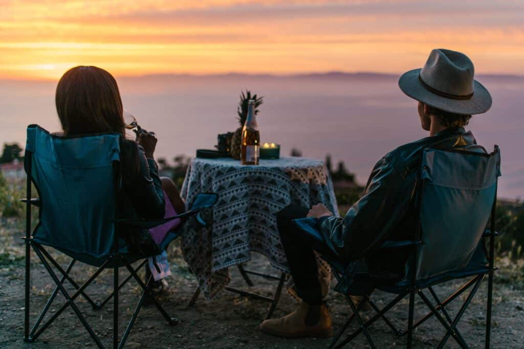 Deux personnes installées autour d’une table face à la mer au coucher du soleil.